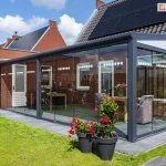 Aluminiowy ogród zimowy ze szkłem przesuwanym i poliwęglanem bocznym na zadaszeniu Lunaro z wygodnymi meblami wewnątrz i ozdobnymi kwiatami na zewnątrz