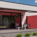 Nowoczesna wizualizacja tarasu przylegającego do budynku o minimalistycznej architekturze z płaskim dachem. Elewacja domu składa się z dwóch tekstur: białego tynku oraz ciemnoszarych, dużych płyt elewacyjnych z poziomymi boniowaniami po lewej stronie. Na tarasie zamontowano system osłon przeciwsłonecznych w intensywnym czerwonym kolorze. Głównym elementem jest szeroka markiza tarasowa kasetowa z ramionami przegubowymi, której poszycie rzuca czerwony cień na jasną ścianę budynku i przeszklenia. Konstrukcja markizy, w tym kaseta i ramiona, wykonana jest z aluminium w kolorze ciemnografitowym. Poniżej, na prawej krawędzi tarasu, znajduje się boczna markiza Bora Selt wyciągana z pionowej kasety, tworząca czerwoną ściankę oddzielającą przestrzeń wypoczynkową. Taras został wyłożony deskami kompozytowymi w kolorze jasnoszarego drewna. Na tarasie ustawiono zestaw mebli ogrodowych typu lounge, składający się z trzech nowoczesnych foteli o metalowej, czarnej konstrukcji z siatkowym siedziskiem oraz niskiego stolika kawowego wykonanego z białej palety transportowej. Duże, przesuwne drzwi tarasowe w czarnych ramy odbijają otaczającą zieleń drzew. Przed tarasem widoczna jest nowoczesna aranżacja ogrodowa z szarym żwirem, w którym posadzono w równych odstępach niskie, zielone krzewy ozdobne. Po lewej stronie znajduje się antracytowa donica z wysokimi trawami ozdobnymi. Całość przedstawiona jest w pełnym słońcu na tle bezchmurnego, niebieskiego nieba.