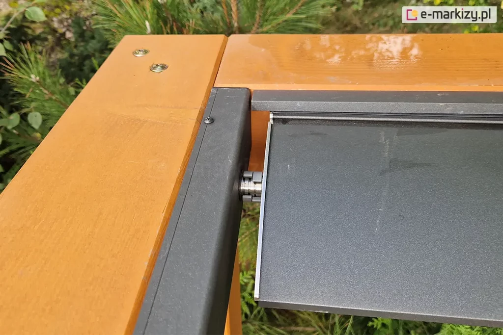 Drewniane belki pergoli, do których zamocowano profile dachu lamelowego SB400 MD Selt z umieszczonym w nim jednym lamelem dachowym w kolorze antracytowym.