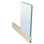 Zdjęcie prezentuje sposób montażu panelu szklanego w systemie przesuwnym Auris z wykorzystaniem dolnego profilu aluminiowego w kolorze kremowo-białym. Przezroczysta tafla szkła o widocznym zielonkawym odcieniu na krawędzi jest wsunięta w kanał profilu, co obrazuje stabilność osadzenia wypełnienia. Profil dolny posiada gładką powierzchnię i jest zakończony widocznym od strony czołowej mechanizmem z wkrętem montażowym oraz otworem technologicznym, co wskazuje na techniczną stronę konstrukcji wózka jezdnego lub systemu blokad. Całość ukazana jest pod kątem na jasnym tle, co pozwala na dokładne zaobserwowanie proporcji między grubością szkła a szerokością profilu trzymającego, a także precyzyjne spasowanie elementów konstrukcyjnych systemu Auris.