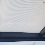 Zbliżenie na płytę z poliwęglanu komorowego w odcieniu mlecznym, zamocowaną w konstrukcji zadaszenia o antracytowym kolorze.