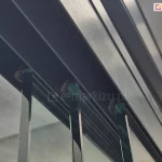 Zbliżenie mocowania paneli szklanych bezramowego systemu Miros w górnej prowadnicy. Widoczne uszczelki szczotkowe na zakończeniach paneli ze szkła, które zapobiegają przedostawaniu się na taras owadów oraz ograniczają przeciągi.
