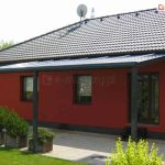 Nowoczesna konstrukcja zadaszenia z poliwęglanu w kolorze dachu budynku na tle ciemnoczerwonej ściany elewacji