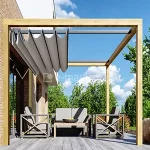 Wizualizacja nowoczesnej pergoli tarasowej Koro o konstrukcji drewnianej, zamontowanej przy elewacji budynku wykonanej z jasnej cegły. Pergola posiada formę minimalistycznego sześcianu zbudowanego z grubych belek z jasnego drewna o wyraźnym usłojeniu. Zadaszenie stanowi system rzymskiedo dachu Silva z tkaniną w kolorze jasnoszarym, która jest częściowo zwinięta przy ścianie budynku, tworząc dekoracyjne, faliste fałdy materiału zawieszone na poziomych prowadnicach. Pod pergolą zaaranżowano strefę wypoczynkową z meblami ogrodowymi: dwoma fotelami i sofą w szarym odcieniu z drewnianymi akcentami na bokach w kształcie litery X oraz niskim stolikiem kawowym, na którym stoi miska z owocami. Podłoga tarasu wykonana jest z szerokich, szarych desek kompozytowych. W tle widoczny jest słoneczny ogród z gęstymi, zielonymi drzewami oraz błękitne niebo z rozproszonymi, białymi chmurami. Całość ujęcia prezentuje estetyczne połączenie naturalnych materiałów z nowoczesnym designem systemów przeciwsłonecznych.