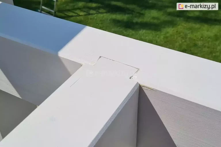 Zbliżenie na sposób łączenia belek konstrukcji, montaż pergoli drewnianej model Moza na zakładki. W tle zielony trawnik.