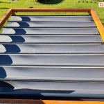 Pergola drewniana Koro z rozwiniętym dachem Supro z tkaniną Opatex o antracytowym kolorze od zewnątrz na tarasie z widocznym zielonym trawnikiem.