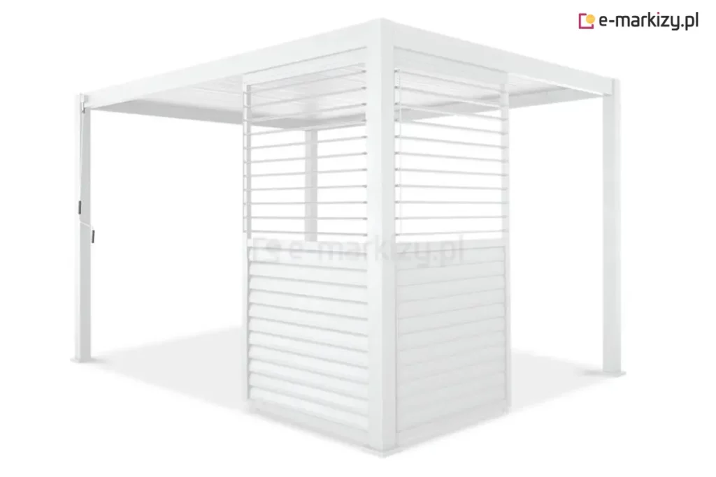 Biała pergola ogrodowa Gloria z narożną zabudową wykonaną z dwóch ruchomych paneli żaluzjowych typu shutters. Panele zamontowane są prostopadle do siebie przy jednym ze słupów nośnych, tworząc częściową osłonę kątową. Każdy moduł posiada konstrukcję podzieloną na dwie sekcje pionowe: dolna wypełniona jest lamelami w pozycji całkowicie zamkniętej, tworząc nieprzezierną płaszczyznę, natomiast w górnej sekcji lamele są ustawione poziomo, co zapewnia prześwit i widoczność. Cała konstrukcja, w tym dach lamelowy, cztery słupy z kwadratowymi stopami oraz ramy osłon, jest polakierowana na jednolity biały kolor. Po lewej stronie, na przednim słupie, widoczny jest pionowy drążek mechanizmu korbowego do obsługi zadaszenia.