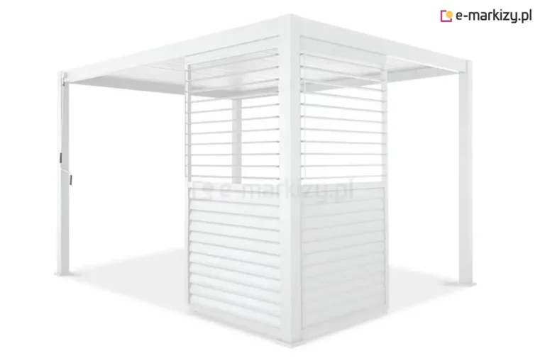 Biała pergola ogrodowa Gloria z narożną zabudową wykonaną z dwóch ruchomych paneli żaluzjowych typu shutters. Panele zamontowane są prostopadle do siebie przy jednym ze słupów nośnych, tworząc częściową osłonę kątową. Każdy moduł posiada konstrukcję podzieloną na dwie sekcje pionowe: dolna wypełniona jest lamelami w pozycji całkowicie zamkniętej, tworząc nieprzezierną płaszczyznę, natomiast w górnej sekcji lamele są ustawione poziomo, co zapewnia prześwit i widoczność. Cała konstrukcja, w tym dach lamelowy, cztery słupy z kwadratowymi stopami oraz ramy osłon, jest polakierowana na jednolity biały kolor. Po lewej stronie, na przednim słupie, widoczny jest pionowy drążek mechanizmu korbowego do obsługi zadaszenia.