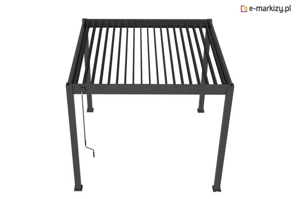 Zdjęcie przedstawia wolnostojącą pergolę tarasową Marlo w kolorze antracytowym, ukazaną z perspektywy górnej, co pozwala na dokładny wgląd w konstrukcję dachu lamelowego. Aluminiowa rama o kwadratowym profilu wspiera system ruchomych lameli, które na fotografii są ustawione w pozycji otwartej, tworząc równoległe szczeliny przepuszczające światło. Na jednym z przednich słupów bocznych zamontowany jest mechanizm korbowy z długim drążkiem, przeznaczony do ręcznej regulacji kąta nachylenia piór dachu. Konstrukcja opiera się na czterech pionowych nogach zakończonych stopami montażowymi, a całe zadaszenie ma formę płaskiego, geometrycznego prostopadłościanu o matowym wykończeniu.