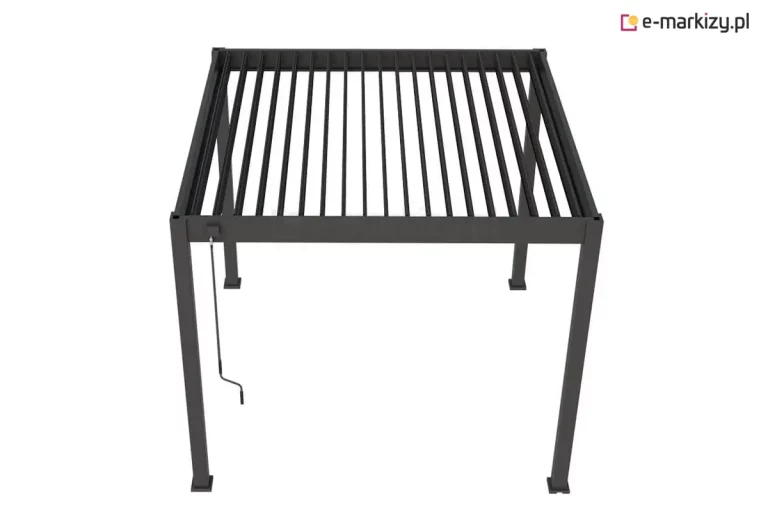 Zdjęcie przedstawia wolnostojącą pergolę tarasową Marlo w kolorze antracytowym, ukazaną z perspektywy górnej, co pozwala na dokładny wgląd w konstrukcję dachu lamelowego. Aluminiowa rama o kwadratowym profilu wspiera system ruchomych lameli, które na fotografii są ustawione w pozycji otwartej, tworząc równoległe szczeliny przepuszczające światło. Na jednym z przednich słupów bocznych zamontowany jest mechanizm korbowy z długim drążkiem, przeznaczony do ręcznej regulacji kąta nachylenia piór dachu. Konstrukcja opiera się na czterech pionowych nogach zakończonych stopami montażowymi, a całe zadaszenie ma formę płaskiego, geometrycznego prostopadłościanu o matowym wykończeniu.