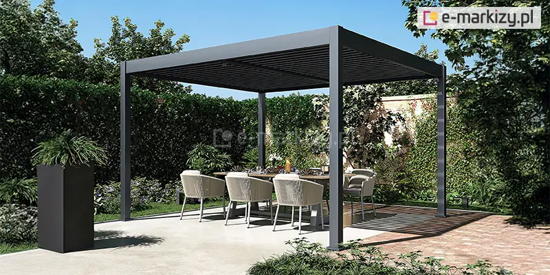 Wolnostojąca pergola lamelowa Marlo Duo o aluminiowej konstrukcji w kolorze ciemnego grafitu, ustawiona w gęsto obsadzonym roślinami ogrodzie. Konstrukcja posiada cztery kwadratowe słupy nośne oraz dach z poziomych, ciemnych lameli. Pod zadaszeniem zaaranżowano jadalnię na świeżym powietrzu z dużym prostokątnym stołem o jasnym blacie, przy którym stoi sześć kubełkowych foteli z jasnobeżowej plecionki z białymi poduszkami na siedziskach. Podłoże pod pergolą jest zróżnicowane – część stanowi jasna, gładka wylewka betonowa, a część nawierzchnia z kostki brukowej w odcieniach brązu i beżu. W tle widoczny jest wysoki, gęsty żywopłot oraz różnorodne krzewy i drzewa liściaste, które szczelnie wypełniają przestrzeń za pergolą. Po lewej stronie, na pierwszym planie, stoi wysoka, prostopadłościenna donica w kolorze czarnym z ozdobną zieloną rośliną. Całość kompozycji skąpana jest w jasnym świetle słonecznym, a na podłożu widoczne są wyraźne pasy cieni rzucane przez lamelowy dach konstrukcji.
