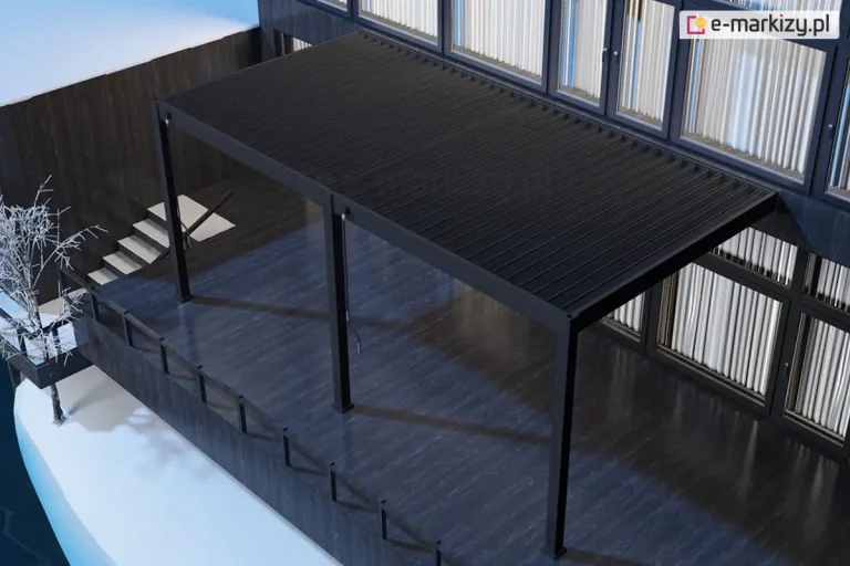 Dwumodułowa pergola lamelowa Marlo w kolorze antracytowym, zamontowana do elewacji nowoczesnego budynku z dużymi przeszkleniami. Konstrukcja składa się z dwóch połączonych sekcji zadaszenia, które wspierają się na trzech pionowych słupach o kwadratowym przekroju, ustawionych w jednej linii od frontu. Lamele dachowe są całkowicie zamknięte, tworząc jednolitą, ciemną płaszczyznę chroniącą rozległy taras. Taras został wykonany z ciemnych desek o wyraźnym połysku, a jego krawędź zabezpieczono minimalistyczną, ciemną balustradą. Po lewej stronie widoczne są schody prowadzące na niższy poziom oraz dekoracyjne, bezlistne drzewko w białym kolorze, co sugeruje zimową lub wczesnowiosenną scenerię z zalegającym gdzieniegdzie śniegiem. Całość ujęcia wykonana jest z perspektywy górnej (z lotu ptaka), co pozwala dokładnie ocenić skalę podwójnego zadaszenia oraz jego integrację z bryłą budynku i otoczeniem.