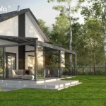 Nowoczesna pergola tarasowa Tarasola Elegancy w formie ogrodu zimowego, zamontowana do białej elewacji domu z dwuspadowym dachem. Konstrukcja pergoli w kolorze antracytowym posiada w pełni przeszklone ściany boczne w systemie przesuwnym oraz zadaszenie tkaninowe rzymskie, które jest rozłożone. Wewnątrz przeszklonej zabudowy znajduje się strefa relaksu z jasnymi, miękkimi pufami oraz stolikiem kawowym, a w dalszej części widoczny jest zestaw mebli jadalnianych. Taras został wykonany z jasnych płyt betonowych z wbudowanym punktowym oświetleniem LED w stopniach schodowych. Budynek posiada charakterystyczne ciemne pionowe pasy na elewacji, które komponują się z kolorem ramy pergoli. Całość zlokalizowana jest w otoczeniu dużego, zielonego trawnika oraz wysokich brzóz, za którymi widoczne jest metalowe ogrodzenie panelowe. Światło słoneczne odbija się w szklanych taflach zabudowy, podkreślając transparentność konstrukcji.