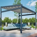 Wolnostojąca pergola rzymska Moderno z tkaninowym dachem tworzy elegancką, otwartą przestrzeń wypoczynkową na podwyższonym tarasie z jasnymi, modułowymi meblami ogrodowymi. Minimalistyczna konstrukcja w antracytowym kolorze harmonizuje z zielenią ogrodu oraz nowoczesnym otoczeniem.