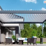 Wizualizacja nowoczesnej pergoli tarasowej w wersji przyściennej, zamontowanej na tarasie wyłożonym jasnymi płytami wielkoformatowymi. Aluminiowa konstrukcja w kolorze ciemnego antracytu składa się z ramy bocznej przytwierdzonej do elewacji budynku oraz ramy frontowej wspartej na jednym widocznym słupie nośnym o kwadratowym przekroju. Zadaszenie bioklimatyczne tworzą białe, ruchome lamele, które na ujęciu są ustawione w pozycji pionowej (otwartej), co pozwala na swobodny przepływ powietrza i maksymalne doświetlenie tarasu. Pod pergolą znajduje się komplet mebli wypoczynkowych z ciemnymi, ażurowymi ramami i białymi poduszkami z błękitnymi akcentami, ustawiony wokół niskiego stolika kawowego. Budynek charakteryzuje się nowoczesną architekturą z elewacją wykonaną z szarej cegły i białego tynku oraz dużymi przeszkleniami. W tle widoczna jest gęsta ściana zielonych drzew liściastych oraz drewniane ogrodzenie panelowe, a nad całością rozciąga się pogodne, jasnoniebieskie niebo z delikatnymi chmurami. W aranżacji uwzględniono również rośliny doniczkowe, w tym wysoką palmę w czarnej, smukłej donicy, co podkreśla relaksacyjny charakter miejsca.