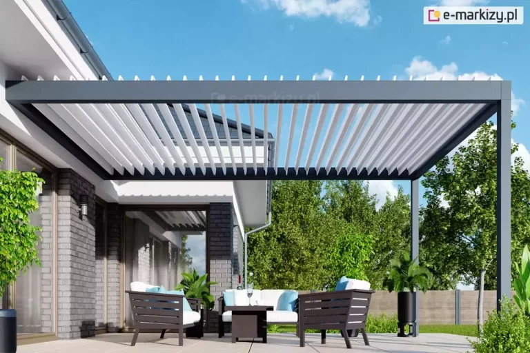 Wizualizacja nowoczesnej pergoli tarasowej w wersji przyściennej, zamontowanej na tarasie wyłożonym jasnymi płytami wielkoformatowymi. Aluminiowa konstrukcja w kolorze ciemnego antracytu składa się z ramy bocznej przytwierdzonej do elewacji budynku oraz ramy frontowej wspartej na jednym widocznym słupie nośnym o kwadratowym przekroju. Zadaszenie bioklimatyczne tworzą białe, ruchome lamele, które na ujęciu są ustawione w pozycji pionowej (otwartej), co pozwala na swobodny przepływ powietrza i maksymalne doświetlenie tarasu. Pod pergolą znajduje się komplet mebli wypoczynkowych z ciemnymi, ażurowymi ramami i białymi poduszkami z błękitnymi akcentami, ustawiony wokół niskiego stolika kawowego. Budynek charakteryzuje się nowoczesną architekturą z elewacją wykonaną z szarej cegły i białego tynku oraz dużymi przeszkleniami. W tle widoczna jest gęsta ściana zielonych drzew liściastych oraz drewniane ogrodzenie panelowe, a nad całością rozciąga się pogodne, jasnoniebieskie niebo z delikatnymi chmurami. W aranżacji uwzględniono również rośliny doniczkowe, w tym wysoką palmę w czarnej, smukłej donicy, co podkreśla relaksacyjny charakter miejsca.