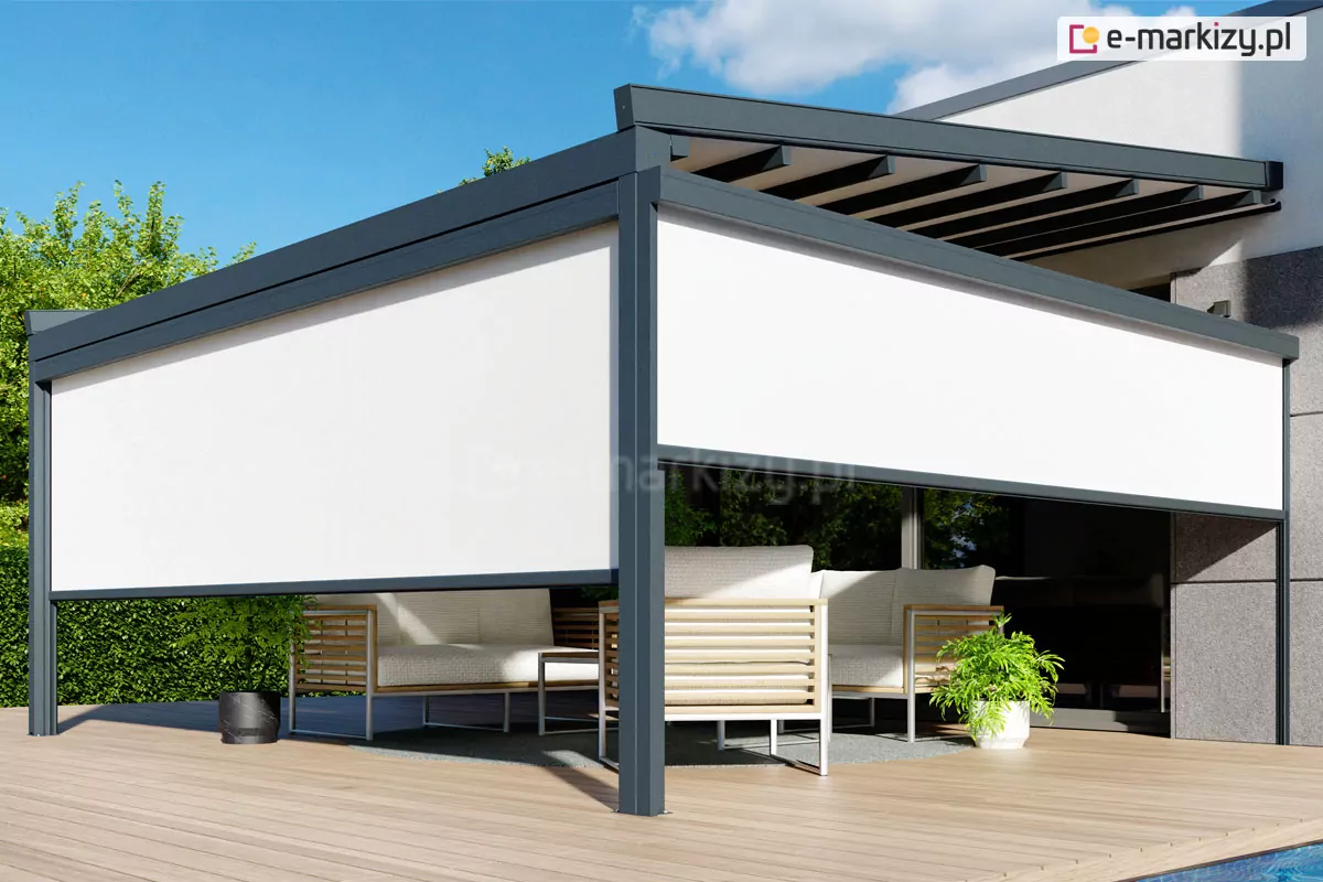 Nowoczesna pergola tarasowa Square o antracytowej, wykonanej z aluminium konstrukcji, wyposażona w białe przesłony boczne typu screen. Przesłony są częściowo opuszczone, zasłaniając górną połowę prześwitów między słupami i tworząc intymną strefę cienia. Konstrukcja zadaszenia posiada widoczne poprzeczne belki w kolorze ciemnoszarym, a całość jest zamontowana do elewacji nowoczesnego budynku o jasnoszarym i grafitowym wykończeniu. Pod pergolą znajduje się luksusowy zestaw mebli ogrodowych z jasnymi poduszkami i drewnianymi elementami wykończeniowymi na podłokietnikach. Na jasnym, drewnianym tarasie ustawione są również donice z zielonymi roślinami – jedna ciemna po lewej stronie i biała po prawej. W tle widoczny jest gęsty zielony żywopłot oraz fragment basenu w prawym dolnym rogu zdjęcia. Scena przedstawiona jest w pełnym słońcu na tle czystego, błękitnego nieba.
