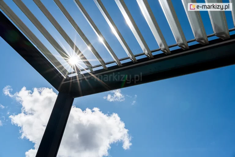 Pergola tarasowa SB 400 Selt z antracytową konstrukcja oraz otwartym dachem panelowym z białych lameli, przepuszczającym promienie słoneczne na tle błękitnego nieba z pierzastymi białymi chmurkami.