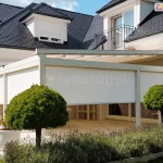 Nowoczesny piętrowy budynek mieszkalny o białej elewacji i grafitowym dachu z dużym tarasem w narożniku, osłoniętym pergolą z roletami screen ZIP L ZIP U. Całość została dopasowana kolorystycznie do elewacji budynku. Przed tarasem zadbany kwietnik z polem lawendy oraz dwoma niskimi drzewami. Przy zejściu z tarasu na trawnik ustawiono dwie duże białe donice z kwiatami.