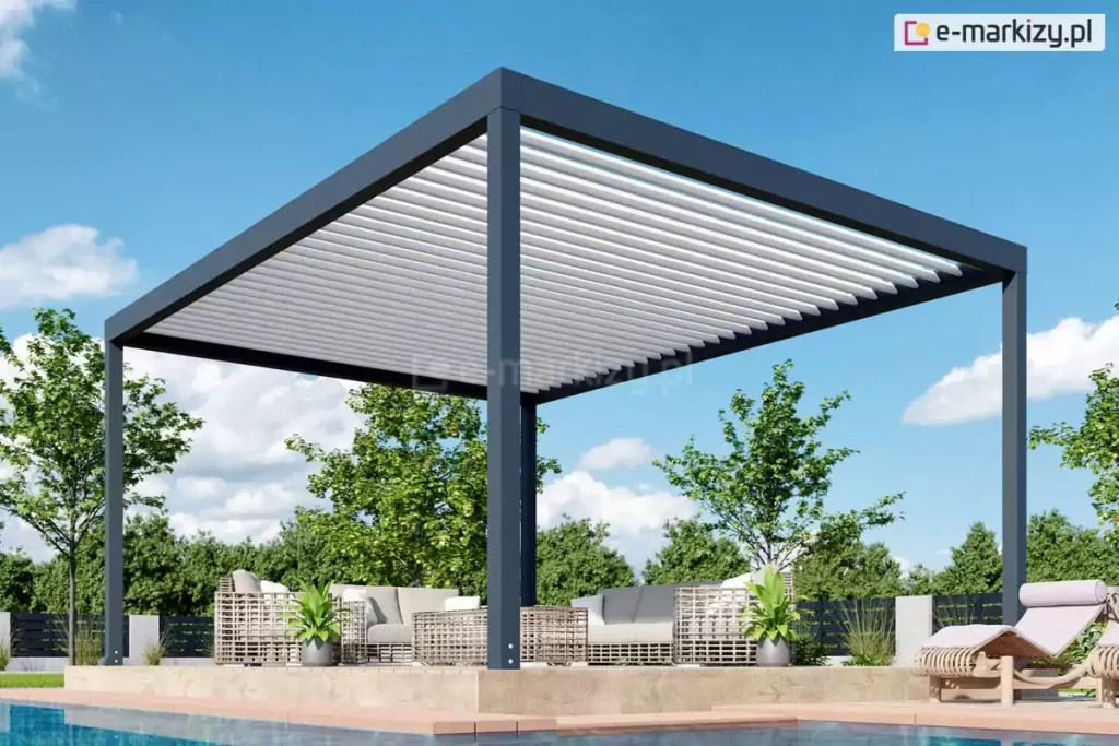 Pergola lamelowa wolnostojąca Bioline, bioklimatyczna o nowoczesnej, geometrycznej konstrukcji, ustawiona na podwyższonym tarasie przy basenie. Aluminiowa konstrukcja pergoli w kolorze głębokiego antracytu składa się z grubych profili ramowych oraz czterech masywnych słupów nośnych o kwadratowym przekroju. Zadaszenie tworzy system poziomych, białych lameli, które są ustawione pod kątem, pozwalając na regulację dopływu światła słonecznego. Pod pergolą znajduje się luksusowa strefa wypoczynkowa wyposażona w meble ogrodowe z technorattanu o jasnej plecionce i szarych poduchach, w tym sofy oraz stolik kawowy. Po bokach mebli ustawiono symetrycznie donice z zielonymi roślinami o podłużnych liściach. Taras wykonany jest z płyt o teksturze jasnego kamienia lub betonu i sąsiaduje bezpośrednio z krawędzią basenu z czystą, błękitną wodą. W tle widoczna jest gęsta ściana zieleni złożona z drzew i krzewów liściastych oraz czarne, nowoczesne ogrodzenie panelowe. Całość kompozycji dopełnia bezchmurne, jasnoniebieskie niebo z delikatnymi, białymi obłokami, co podkreśla letni i wypoczynkowy charakter prezentowanej architektury ogrodowej.