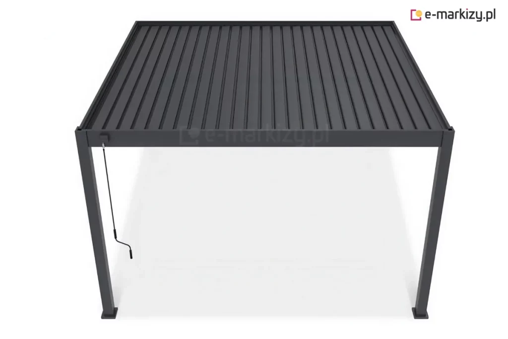 Nowoczesna pergola tarasowa z dachem lamelowym sterowanym ręcznie przedstawiona na jednolitym białym tle. Całość konstrukcji, obejmująca cztery pionowe słupy nośne oraz ramę zadaszenia, wykonana jest z aluminium w głębokim, matowym odcieniu ciemnej szarości lub antracytu. Zadaszenie składa się z równolegle ułożonych, podłużnych lameli, które tworzą szczelną, żebrowaną płaszczyznę dachową. Lamele są osadzone wewnątrz solidnej, prostokątnej ramy. Na przednim lewym słupie, tuż pod górną belką, zamontowany jest mechanizm sterujący w formie zwisającej, czarnej korby z rączką, służącej do manualnej regulacji kąta nachylenia piór dachu. Słupy wspierające mają kwadratowy przekrój i są zakończone u dołu płaskimi stopami montażowymi, które stabilizują konstrukcję na podłożu. Perspektywa ujęcia ukazuje produkt z lekkiego podwyższenia, co pozwala dokładnie przyjrzeć się strukturze zamkniętego dachu oraz proporcjom całej wolnostojącej budowli ogrodowej.