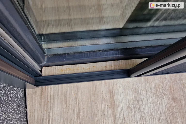 Ujęcie z góry progu moskitiery plisowanej Top Zag z widocznymi w nim sznurkami. Prowadnice boczne przymocowane zostały do prowadnic rolety zewnętrznej.