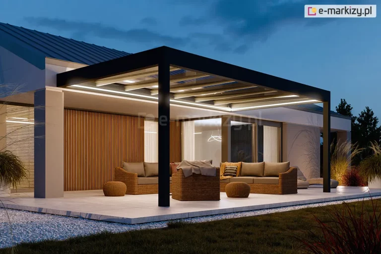 Wieczorna ekspozycja nowoczesnego zadaszenia tarasowego Spekta Glass, zintegrowanego z bryłą budynku jednorodzinnego o jasnej elewacji. Konstrukcja nośna została wykonana z grubych profili aluminiowych w kolorze antracytowym, które tworzą geometryczną ramę wspartą na pionowych słupach. System został wyposażony w zintegrowane oświetlenie LED w formie intensywnych, liniowych pasów świetlnych zamontowanych wzdłuż ramy obwodowej, które oświetlają całą strefę wypoczynku. Wewnątrz przeszklonej strefy zaaranżowano komfortowe miejsce do relaksu z kompletem mebli z technorattanu: dwiema sofami, fotelem z brązowymi poduchami oraz niskimi, okrągłymi pufami. Ściana budynku pod zadaszeniem została wykończona dekoracyjnymi, pionowymi lamelami drewnianymi, co podkreśla nowoczesny design. Podłoże stanowią wielkoformatowe płyty tarasowe w jasnym odcieniu, otoczone pasem białego gresu i ciemnym trawnikiem. Całość kompozycji, dopełniona przez nastrojowe oświetlenie ogrodowe i roślinność w tle, tworzy luksusową i spójną przestrzeń wypoczynku.