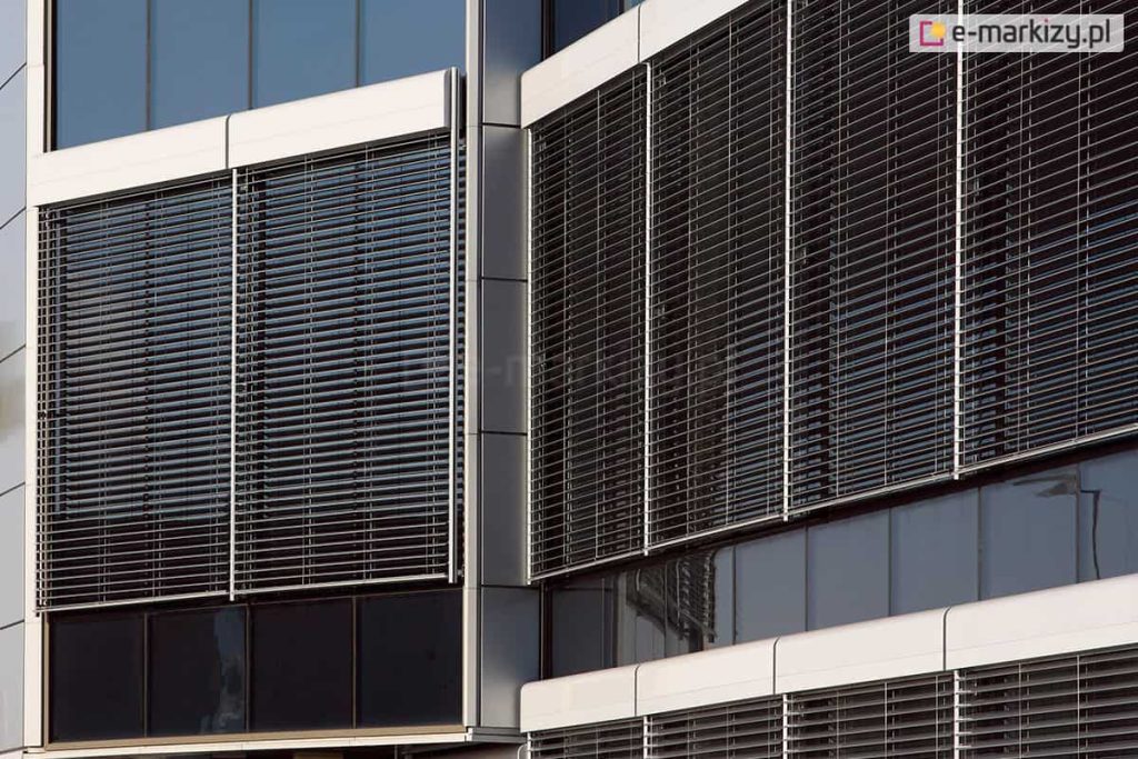 Oszklony budynek osłonięty żaluzjami fasadowymi z kasetą oval zamontowanymi modułowo.