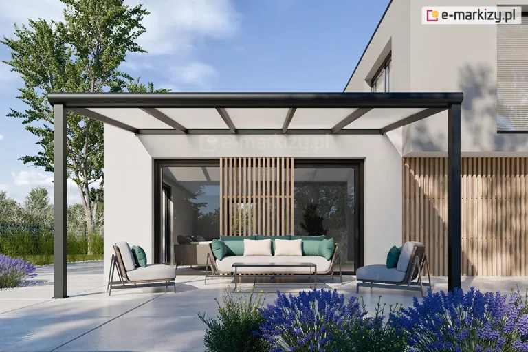 Nowoczesne zadaszenie tarasowe Lunaro w kolorze antracytowym, zamontowane do jasnej elewacji minimalistycznego, piętrowego budynku. Konstrukcja dachu opiera się na poprzecznych aluminiowych krokwiach z wypełnieniem z mlecznych paneli poliwęglanowych, a całość wspierają dwa smukłe, kwadratowe słupy nośne ustawione na brzegach tarasu. Na pierwszym planie widoczne są intensywnie fioletowe kwiaty lawendy, a w tle wysokie drzewa liściaste pod jasnym, pogodnym niebem. Pod zadaszeniem, na jasnej i gładkiej nawierzchni, zaaranżowano strefę relaksu z designerską sofą ozdobioną miętowo-beżowymi poduszkami, dwoma fotelami w podobnym stylu oraz niskim, prostokątnym stolikiem kawowym. Przeszklone wejście do domu zdobią pionowe, drewniane lamele, które pełnią funkcję dekoracyjną i osłonową.