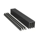 Zdjęcie prezentuje zestaw dwóch profili aluminiowych stanowiących elementy 3-torowego systemu przesuwnego Auris, przedstawionych na białym tle. Po prawej stronie widoczna jest prowadnica górna o głębokim, prostokątnym przekroju z trzema wyraźnie wydzielonymi komorami wewnętrznymi, wykończona w matowym kolorze antracytowym. Po lewej stronie znajduje się niższa prowadnica dolna, która posiada trzy równoległe szyny jezdne o charakterystycznym, wypukłym kształcie, przystosowanym do poruszania się po nich rolek wózków jezdnych. Oba profile są ustawione pod kątem, co pozwala na dokładne przyjrzenie się budowie wewnętrznej oraz grubości ścianek aluminium. Powierzchnia produktów charakteryzuje się drobną strukturą, typową dla malowania proszkowego stosowanego w nowoczesnych systemach zabudowy tarasów.