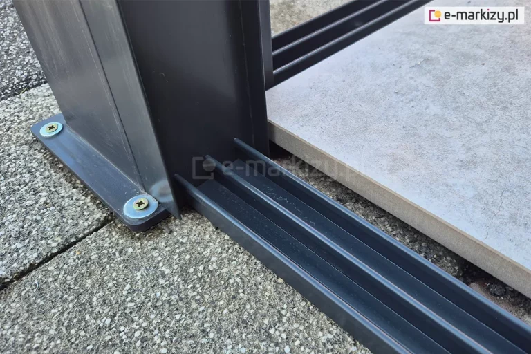 Prowadnica dolna z trzema torami w kolorze antracytowym zamocowana do podłoża z płyt betonowych przy tarasie.