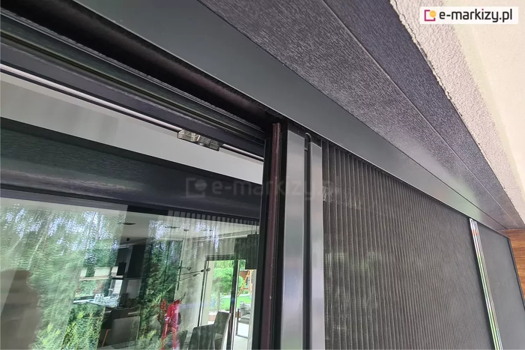 Górny profil moskitiery Click Rol stanowi ukrytą prowadnicę, w której porusza się profil z siatką oraz gąsienice. Moskitiera z antracytową konstrukcją zamocowana na oknie w tej samej kolorystyce.