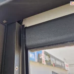 Słupek konstrukcji pergoli sb 400 Selt w kolorze antracytowym z zamontowaną refleksolą ziiip 120 umieszczoną w prowadnicy bocznej. Konstrukcja refleksola dopasowana została do koloru pergoli, w belce dolnej widoczna uszczelka szczotkowa oraz zwinięta tkanina screen w kolorze beżowym.