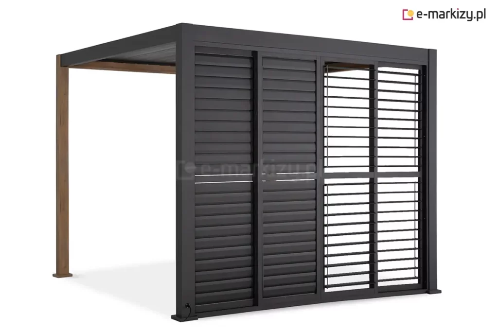 Antracytowa pergola Gloria z systemem przesuwnych paneli żaluzjowych, przedstawiona w ujęciu od strony frontu. Zabudowa składa się z czterech skrzydeł, które są przesunięte w prawą stronę, pozostawiając lewą część boku pergoli otwartą. Dwa panele po lewej stronie mają lamele ustawione w pozycji całkowicie zamkniętej, tworząc jednolitą osłonę. Dwa panele po prawej stronie mają lamele ustawione poziomo, co pozwala na swobodny przepływ światła i wgląd do wnętrza. Każde skrzydło posiada aluminiową ramę z poprzeczką dzielącą panel na dwie równe sekcje pionowe. Konstrukcja pergoli opiera się na ciemnych słupach przednich oraz tylnych słupach o strukturze imitującej drewno. W dolnej części lewego słupa widoczne jest gniazdo z podłączonym przewodem zasilającym.
