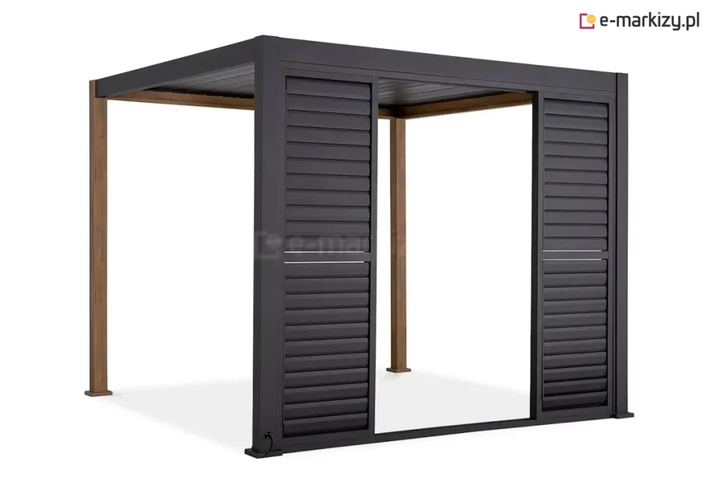 Antracytowa pergola Gloria z systemem przesuwnych shuttersów, zamontowanych na jednym z boków konstrukcji. Na zdjęciu widoczne są dwa panele żaluzjowe rozsuniecie na boki, które tworzą szerokie światło przejścia w środkowej części. Każdy panel składa się z dwóch sekcji wypełnionych poziomymi, nieruchomymi lamelami o szerokim profilu, które zapewniają ochronę przed słońcem i prywatność. Rama pergoli oraz panele przesuwne są wykonane z aluminium w kolorze ciemnoantracytowym, natomiast dwa tylne słupy konstrukcyjne mają wykończenie w kolorze naturalnego drewna. W lewym dolnym rogu przedniego słupa widoczne jest wyprowadzenie przewodu elektrycznego. Całość osadzona jest na stabilnych stopach montażowych, a dach konstrukcji tworzą dopasowane kolorystycznie lamele.