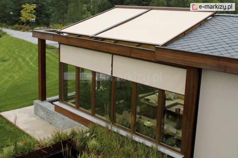 Przeszklone patio nowoczesnego domu z roletami zewnętrznymi typu ZIP L zamontowanymi na dużych, drewnianych ramach okiennych. Rolety w jasnym, beżowym kolorze osłaniają wnętrze ogrodu zimowego, zapewniając prywatność i ochronę przed słońcem. Konstrukcja dachu wykonana z drewna łączy się z fragmentem dachu pokrytego grafitową dachówką. Przeszkloną część dachu osłonięto roletami poziomymi w kolorystyce dopasowanej do stylu i barw domu. Wewnątrz pomieszczenia widoczne są rośliny doniczkowe oraz zestaw wypoczynkowy z kanapą i stolikiem. Otoczenie domu stanowi zadbany trawnik, roślinność ozdobna i alejka z kamienną nawierzchnią prowadząca przez ogród.