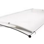 Zdjęcie prezentuje model zadaszenia drzwiowego Elegant z wypełnieniem w formie płyty akrylowej o przymglonym, lekko matowym wykończeniu, które subtelnie rozprasza światło. Tafla o łukowatym kształcie jest zamontowana na srebrnym, metalowym wsporniku o ażurowej konstrukcji z charakterystycznym, podłużnym wycięciem. Na przedniej krawędzi daszka znajduje się aluminiowy profil rynnowy o cylindrycznym kształcie, zakończony ciemną, okrągłą zaślepką. System mocowania płyty do stelaża wykorzystuje punktowy, okrągły uchwyt umieszczony w górnej części ramienia wspornika. Tylna krawędź konstrukcji została wykończona listwą montażową przylegającą do ściany, a całe zadaszenie jest nachylone pod kątem, co ułatwia odprowadzanie opadów do rynny czołowej.