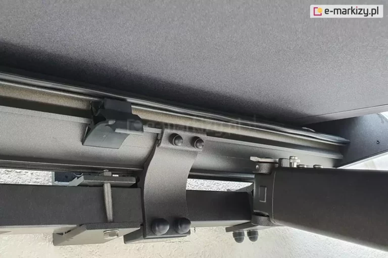 Zbliżenie belki kwadratowej markizy Palladio Selt w kolorze srebrzysty grafit z widocznym po lewej mocowaniem ramienia, uchwytem kasety pośrodku oraz uchwytem ściennym po lewej.