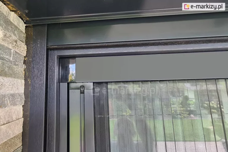 Ramka moskitiery Click ROL z widocznym profilem siatki oraz zaślepką w narożniku, wykonana w kolorze antracytowym, dopasowanym do drewnianej ramy okna w tym samym kolorze.