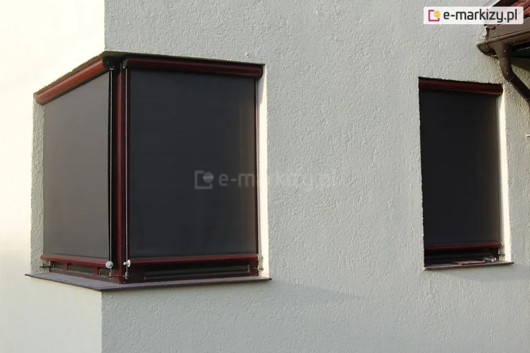 Narożnik budynku o białej fasadzie z widocznymi dwoma oknami: narożnym oraz wąskim okienkiem na prawej ścianie. Oba okna w kolorze brązowym osłonięto refleksolami 125 Selt w kolorystyce konstrukcji i tkaniny zbliżonej do barwy okien. Wszystkie okna są w pełni zasłonięte materiałem rolety screen.