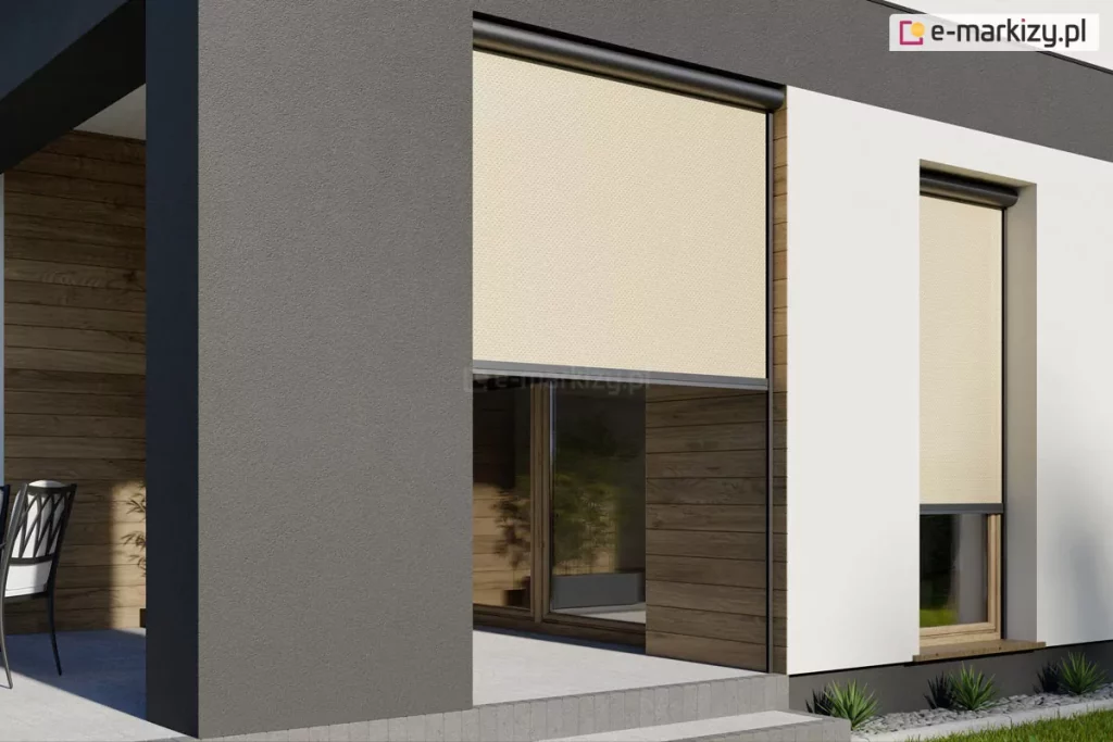 Zdjęcie przedstawia nowoczesną elewację budynku z zamontowanymi osłonami zewnętrznymi typu refleksol 90 Selt. Na zdjęciu widoczne są dwa alternatywne zastosowania refleksoli z konstrukcją w kolorze antracytowym. Lewy refleksol zastosowany został jako przesłona wnęki tarasu, przejścia z ogrodu na taras, które jest przysłonięte w połowie przez beżową tkaninę techniczną o gęstym splocie. Tkanina ta skutecznie rozprasza światło słoneczne, zachowując jednocześnie częściową widoczność wnętrza. Prawy refleksol został zamocowany na tradycyjne okno i posiada niemal całkowicie rozwiniętą roletę w tym samym odcieniu. Kasety rolet o zaokrąglonym profilu są zamontowane w świetle wnęk okiennych, a tkaniny poruszają się wzdłuż dyskretnych prowadnic bocznych. Elewacja domu łączy antracytowy tynk z białymi płaszczyznami oraz wstawkami z naturalnego drewna w ciepłym odcieniu. W tle, za przeszkleniem, widoczne jest stylowe wnętrze z roślinnością, a na zewnątrz fragment tarasu z meblami ogrodowymi oraz starannie przystrzyżony trawnik z ozdobnymi roślinami przy fundamencie budynku. Całość kompozycji podkreśla estetyczny i funkcjonalny charakter refleksoli jako integralnego elementu nowoczesnej architektury.