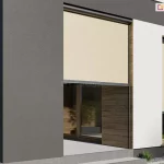 Zdjęcie przedstawia nowoczesną elewację budynku z zamontowanymi osłonami zewnętrznymi typu refleksol 90 Selt. Na zdjęciu widoczne są dwa alternatywne zastosowania refleksoli z konstrukcją w kolorze antracytowym. Lewy refleksol zastosowany został jako przesłona wnęki tarasu, przejścia z ogrodu na taras, które jest przysłonięte w połowie przez beżową tkaninę techniczną o gęstym splocie. Tkanina ta skutecznie rozprasza światło słoneczne, zachowując jednocześnie częściową widoczność wnętrza. Prawy refleksol został zamocowany na tradycyjne okno i posiada niemal całkowicie rozwiniętą roletę w tym samym odcieniu. Kasety rolet o zaokrąglonym profilu są zamontowane w świetle wnęk okiennych, a tkaniny poruszają się wzdłuż dyskretnych prowadnic bocznych. Elewacja domu łączy antracytowy tynk z białymi płaszczyznami oraz wstawkami z naturalnego drewna w ciepłym odcieniu. W tle, za przeszkleniem, widoczne jest stylowe wnętrze z roślinnością, a na zewnątrz fragment tarasu z meblami ogrodowymi oraz starannie przystrzyżony trawnik z ozdobnymi roślinami przy fundamencie budynku. Całość kompozycji podkreśla estetyczny i funkcjonalny charakter refleksoli jako integralnego elementu nowoczesnej architektury.