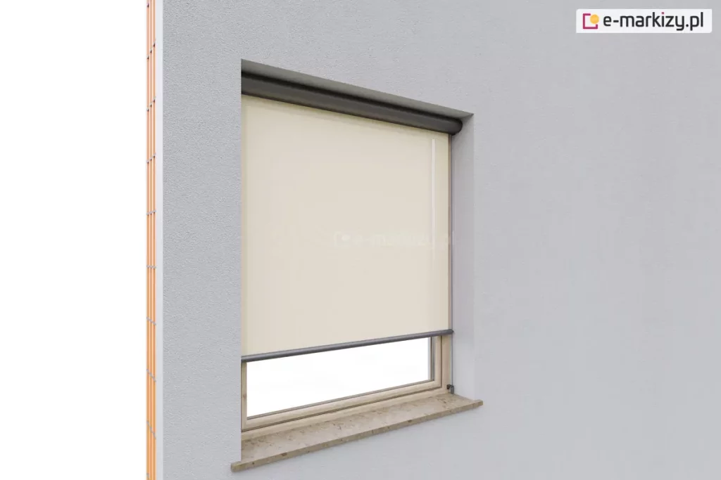 Przekrój pokazujący lewację budynku w trakcie wykańczania, z zamontowaną zewnętrzną osłoną typu Refleksol 90 Selt. Roleta z jasną, beżową tkaniną przeciwsłoneczną została częściowo rozwinięta i przysłania górną część okna osadzonego w szarej elewacji. Zastosowano prowadnice boczne linkowe, mocowane do ramy okna, które stabilizują tkaninę, a całość zamknięta jest w estetycznej kasecie o zaokrąglonym profilu, umieszczonej w górnej części nad wnęką okienną. Kaseta ma grafitowy kolor, co kontrastuje z jasną powierzchnią elewacji i podkreśla nowoczesny charakter rozwiązania. Osłona Refleksol pełni tutaj funkcję ochrony przeciwsłonecznej, a jej subtelny wygląd sprawia, że integruje się wizualnie z bryłą budynku.