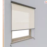 Montaż Refleksola 90 Selt z tkaniną screenową w jasnym kolorze na pojedynczym oknie w elewacji wykończonej szarym tynkiem. Osłona znajduje się w wąskiej kasecie aluminiowej w kolorze grafitowym, która nadaje całości nowoczesny i elegancki wygląd. Tkanina screenowa, wykonana z materiału o drobnym splocie, została rozwinięta do połowy wysokości okna, co pozwala na kontrolę nasłonecznienia bez całkowitego ograniczenia widoku na zewnątrz. Dolna belka rolety jest dopasowana kolorystycznie do kasety i utrzymuje materiał w napięciu, dzięki prowadnicom bocznym linkowym, przymocowanym na wysięgnikach do ściany poza wnęka okienną. Okno osadzone jest w elewacji z wyraźnie widocznym, naturalnym parapetem z kamienia. Refleksol prezentuje się jako praktyczne i estetyczne rozwiązanie, które podnosi komfort cieplny i wizualny budynku.