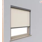 Nowoczesna, elewacyjna osłona przeciwsłoneczna Refleksol 90 Selt zamontowana na pojedynczym oknie zewnętrznym. Roleta wykonana z półprzezroczystej tkaniny w odcieniu jasnego kremu, zamknięta w aluminiowej kasecie w kolorze grafitowym. Konstrukcja rolety obejmuje również prowadnice boczne zamocowane do wnęki okiennej oraz listwę dolną, co zapewnia stabilność materiału i estetyczny wygląd. Okno osadzone jest w ścianie z tynkiem cienkowarstwowym w chłodnym odcieniu szarości, z widocznym fragmentem surowej cegły po lewej stronie.