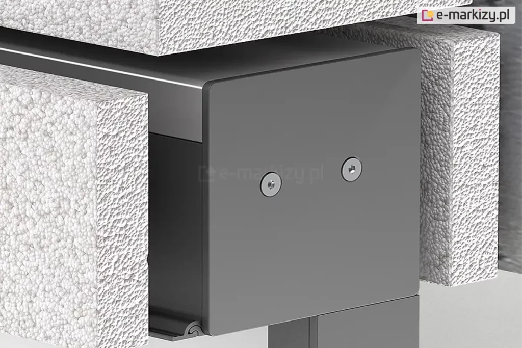 Zbliżenie techniczne na montaż podtynkowy kasety refleksola 120 Ziiip Selt w warstwie termoizolacji budynku. Zdjęcie prezentuje boczną pokrywę (boczek) kasety w kolorze antracytowym, przymocowaną dwiema śrubami z gniazdem typu torx. Kaseta jest precyzyjnie osadzona w wycięciu wykonanym w białym styropianie o wyraźnej strukturze granulatu. Konstrukcja ukazuje sposób integracji systemu osłonowego z elewacją, gdzie górna i boczna część obudowy stykają się bezpośrednio z materiałem izolacyjnym, co pozwala na późniejsze ukrycie mechanizmu pod tynkiem. W dolnej części widoczny jest profil prowadnicy.