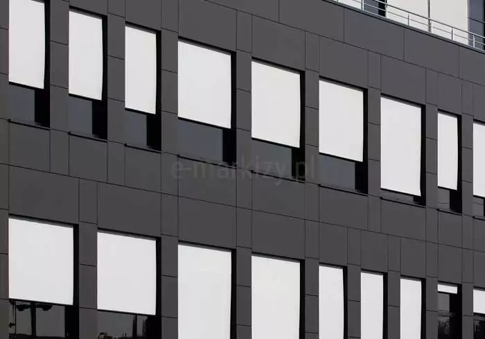 Elewacja nowoczesnego budynku z dużą liczbą prostokątnych okien, na których zamontowano zewnętrzne refleksole podtynkowe. Rolety są całkowicie rozwinięte, wykonane z jasnej tkaniny o wysokim stopniu rozproszenia światła. Kasety rolet oraz prowadnice są wkomponowane w czarne obramowania okien, co tworzy spójny i estetyczny wygląd całej fasady. Tkaniny są napięte i płasko przylegają do prowadnic, co świadczy o systemie typu ZIP, zapewniającym odporność na wiatr i dokładne zaciemnienie.
