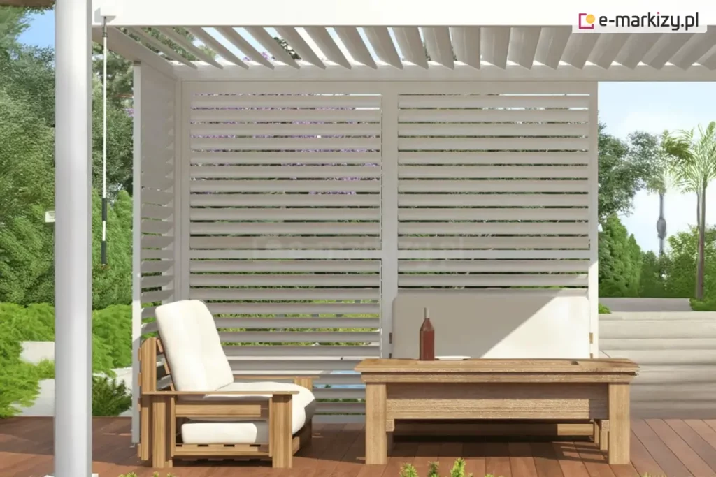 Wnętrze nowoczesnej, białej pergoli lamelowej Gloria wyposażonej w system ruchomych lameli ściennych. Widoczna jest boczna ściana osłonowa składająca się z dwóch dużych paneli wypełnionych poziomymi, białymi lamelami, które są ustawione w pozycji lekko otwartej, co zapewnia prywatność przy jednoczesnym dostępie naturalnego światła i powietrza. Nad przestrzenią wypoczynkową znajduje się dach z lamelami ustawionymi pod kątem, pozwalający na regulację stopnia nasłonecznienia tarasu. Pod pergolą ustawiono stylowe meble ogrodowe wykonane z jasnego drewna: wygodny fotel z grubymi, białymi poduszkami oraz niski stolik kawowy, na którym stoi butelka i kieliszek. Konstrukcja wsparta jest na białym słupie, przy którym widoczna jest korba do ręcznego sterowania mechanizmem. W tle rozpościera się widok na słoneczny ogród z zieloną roślinnością, palmami oraz jasnymi schodami prowadzącymi w głąb posesji.