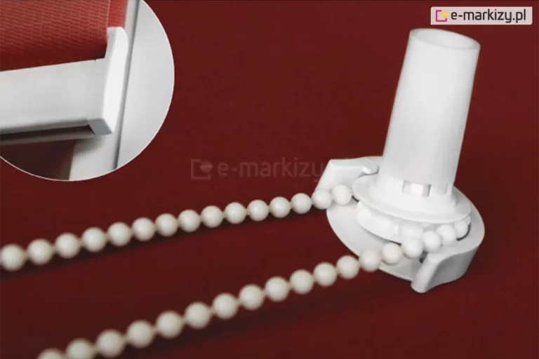 Umieszczony na czerwonym tle mechanizm łańcuszkowy rolety mini w kolorze białym. W lewym górnym rogu w okrągłej ramce zbliżenie belki dolnej, obciążnika tkaniny rolety mini.