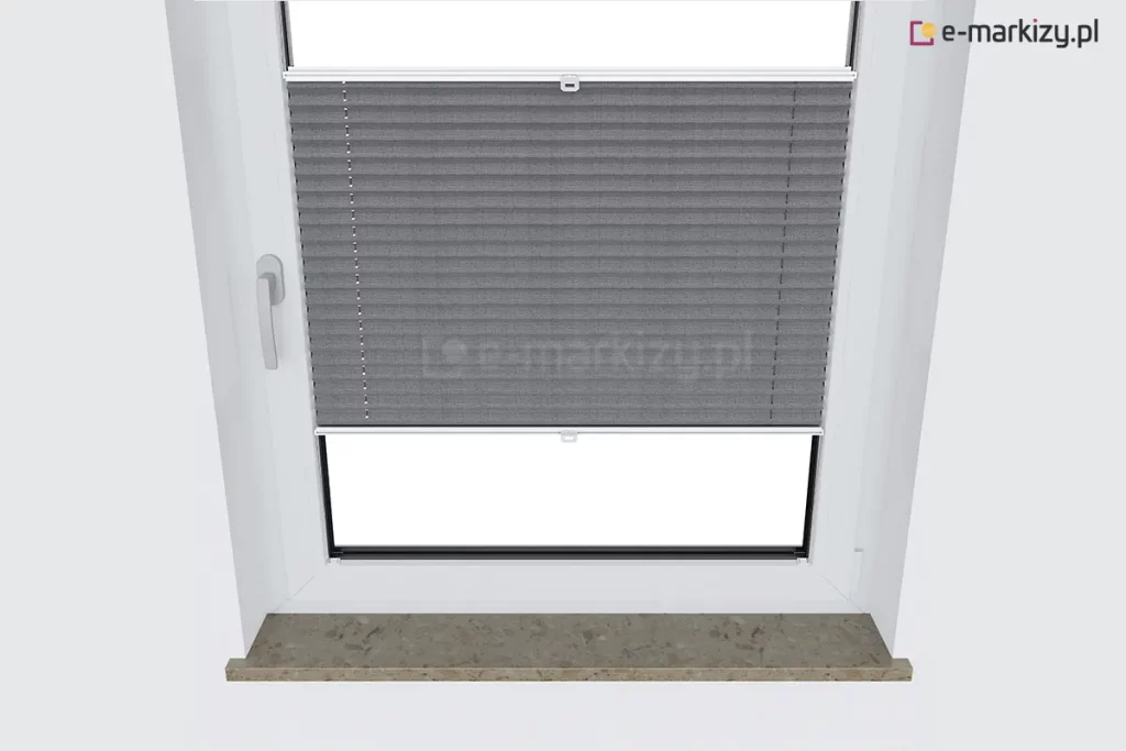 Zdjęcie przedstawia widok z góry na białe okno z zamontowaną nowoczesną osłoną przeciwsłoneczną, którą jest plisa okienna w kolorze ciemnoszarym. Materiał plisy posiada charakterystyczną strukturę harmonijki z regularnymi, poziomymi zagięciami. Osłona jest ustawiona w taki sposób, że zasłania górną i środkową część szyby, odsłaniając jedynie dolny fragment okna. Tkanina jest rozpięta między dwoma białymi profilami aluminiowymi, z których każdy posiada mały, plastikowy uchwyt do regulacji położenia. Przez całą wysokość materiału przechodzą cienkie, pionowe sznurki prowadzące, zapewniające stabilność konstrukcji. Okno osadzone jest w białej wnęce okiennej, a po lewej stronie ramy widoczna jest biała klamka. Pod oknem znajduje się kamienny parapet o matowym wykończeniu w odcieniach beżu i brązu z widocznym nakrapianym wzorem. Perspektywa z góry podkreśla sposób, w jaki plisa okienna przylega do szyby oraz jak estetycznie komponuje się z jasnym wnętrzem i strukturą parapetu.